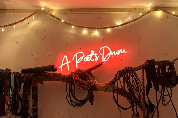 Neon-Schild „A Pato's Drum“ an einer Wand, umgeben von Gurten und einer Lichterkette.